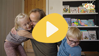To barn som leker med en voksen person foran en bokhylle